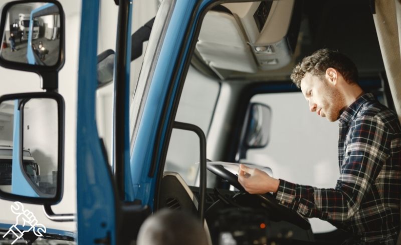 Man seated in a blue truck, focused on driving while checking instruments and mirrors.